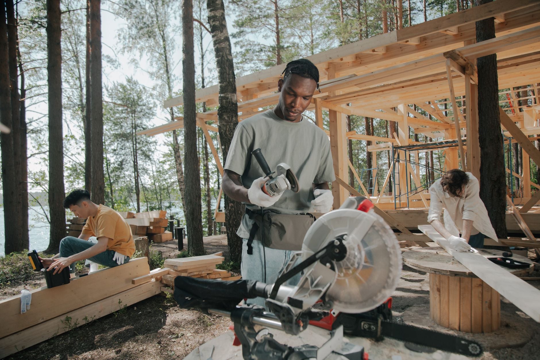 Construction crew building a wooden structure outdoors in a forest setting.